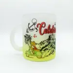 Tazza in vetro satinato con sfumatura gialla, scritta Calabria in rosso corsivo, Vespa verde, ancora nera e edificio costiero su sfondo neutro