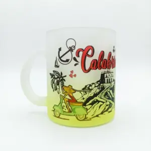 Tazza in vetro satinato con sfumatura gialla, scritta Calabria in rosso corsivo, Vespa verde, ancora nera e edificio costiero su sfondo neutro