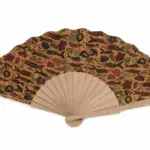 Ventaglio aperto con bacchette in legno chiaro e tessuto beige decorato con pesci stilizzati e fiori in rosso, blu e verde